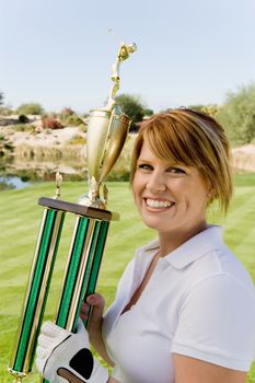 Portrait of a happy female golfer holding trophy on golf course