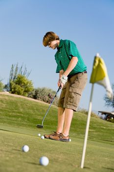 Full Length of a young man concentrating on making putt on golf course