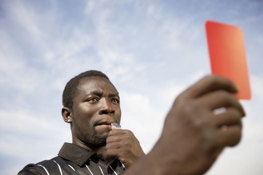 Referee whistles while holding a red card to a player indicating a dismissal