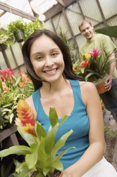 Happy young woman holding potted plant with man in background at botanical garden