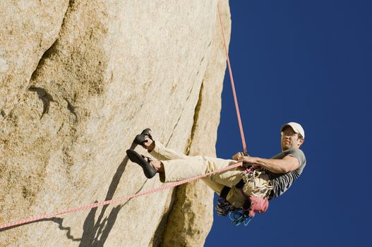 Low angle view of a young man rappelling from cliff