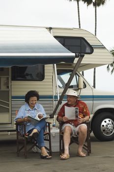 Senior couple sitting on chair with caravan in the background