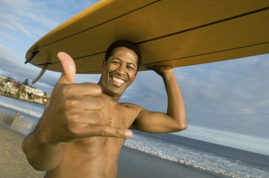 Portrait of an African American man gesturing while carrying surfboard on head