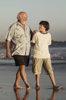 Full length of happy grandfather and grandson walking on beach at dusk