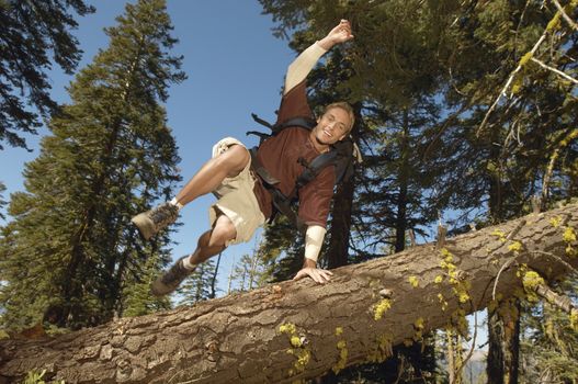 Full length of male hiker jumping over fallen tree in forest