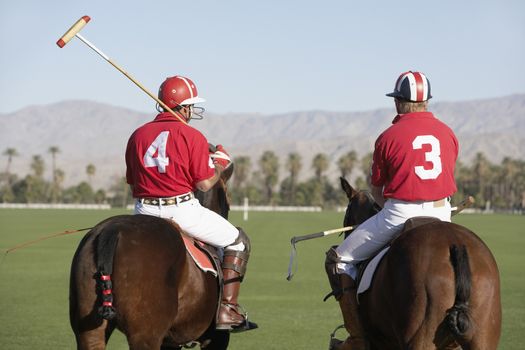Rear view of polo players holding sticks mounted on horses