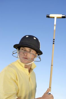 Polo player wearing helmet with polo stick in hand against clear sky