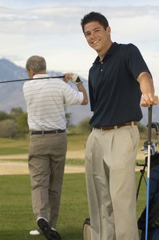Portrait of a happy young male golfer with man playing in background