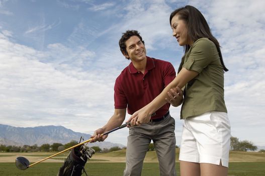 Happy mature man teaching woman to play golf