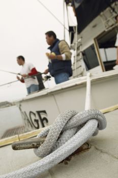 Close up of a rope tied to cleat with men fishing in background
