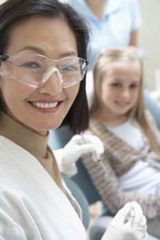 Portrait of a female dentist ready for check-up with little girl sitting in background