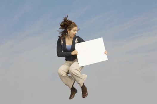 Full length of a mixed race businesswoman in midair holding a blank placard
