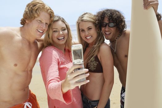 Happy friends taking self-portrait through cell phone on beach