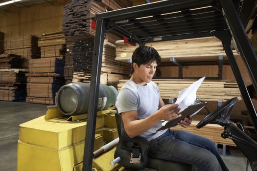 Mid adult worker sitting in forktruck reading documents