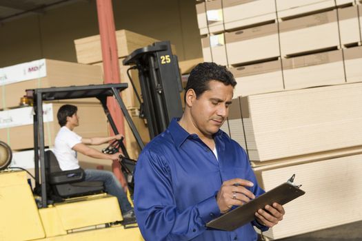Male supervisor with clipboard and forklift truck driver in the background