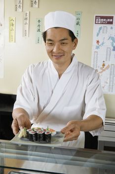 Smiling male chef holding plate of sushi in the restaurant