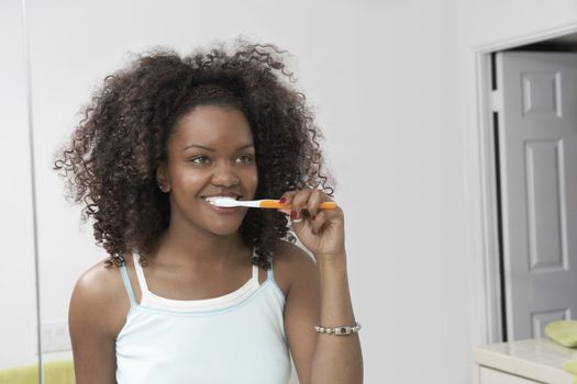 Young African American woman brushing teeth in bathroom