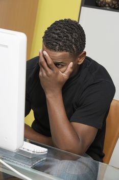 Tensed young African American man looking at desktop PC