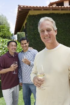 Portrait of happy mature man holding wine glass with friends in background