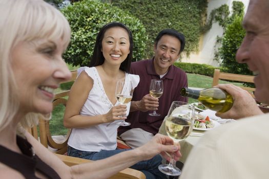 Happy Asian couple looking at man pouring woman glass of wine