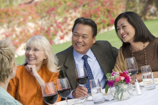 Group of senior friends sitting together drinking wine while looking away