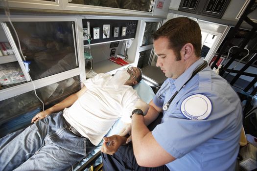 Male EMT professional taking pulse of a man inside ambulance