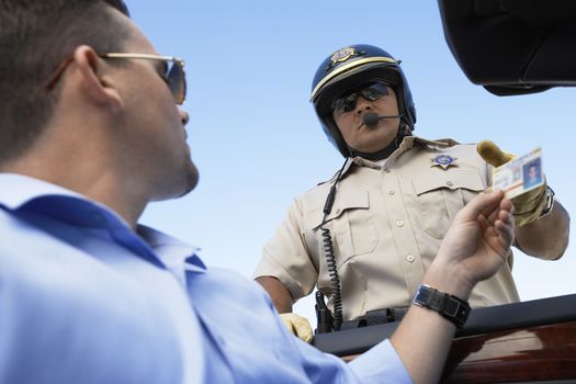 Closeup low angle view of a man handing license to police officer against clear blue sky