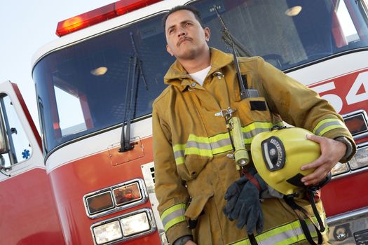 Low angle view of a confident Fire fighter standing in front of fire engine