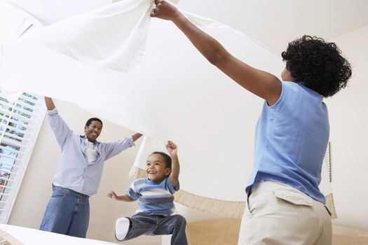 African American parents spreading bedsheet over son in bedroom