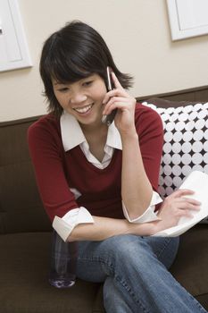 Asian woman sitting on sofa while using cell phone at home