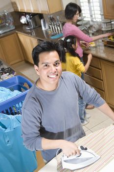 Portrait of a happy man ironing clothes with family in kitchen