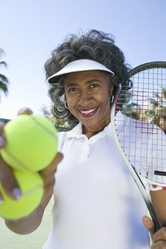 Portrait of a happy senior female tennis player holding racquet and balls