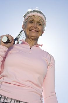 Low angle view of happy senior woman holding tennis racquet against sky