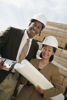 Portrait of two multiethnic surveyors with blueprint on construction site