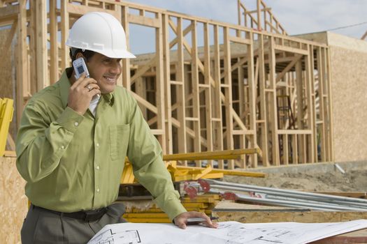 Smiling construction worker with cellphone and blueprints at site