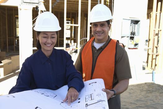 Female architect and co-worker with blueprint at construction site