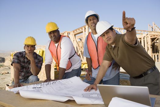 Mature man with team of architects showing something at construction site