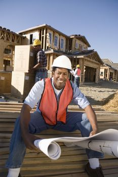 Portrait of a happy architect with blueprint and workers working at construction site
