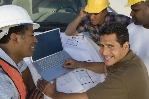 Portrait of a happy mature man with team of architects using laptop