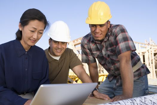 Female architect with workers using laptop at construction site