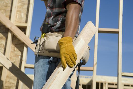 Midsection of a worker holding piece of wood at construction site