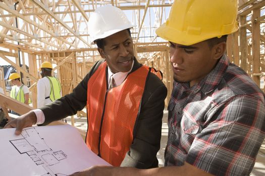 Architect and foreman having discussion over blueprint with workers in background
