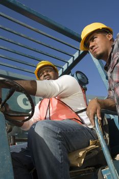 Low angle view of man driving forklift with co-worker standing besides