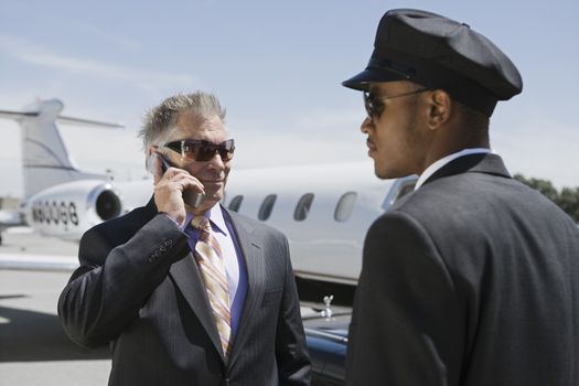 Chauffeur looking at senior businessman on call with private jet in the background
