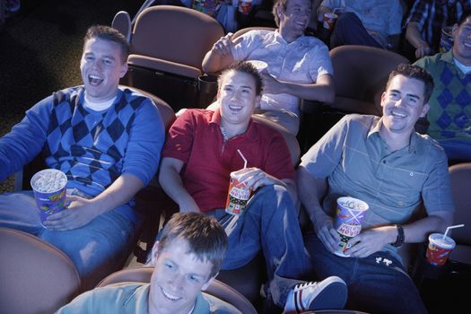 Young men reclining watching movie in theatre smiling