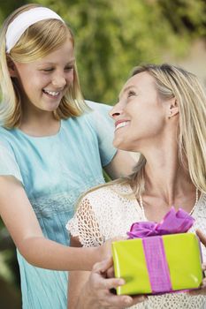 Happy teenage daughter giving present to mother at her birthday