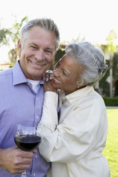 Happy multiethnic couple standing together while man holding wine glass at lawn
