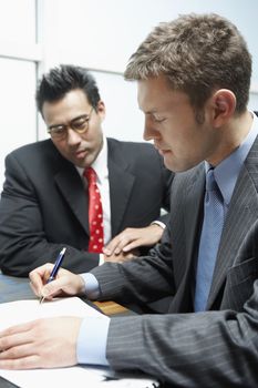 Businessman signing a contract with business partner in the background
