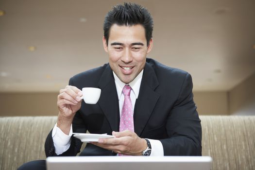 Happy businessman drinking coffee and looking at laptop