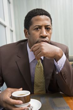 Portrait of a serious African American businessman with coffee cup at office table